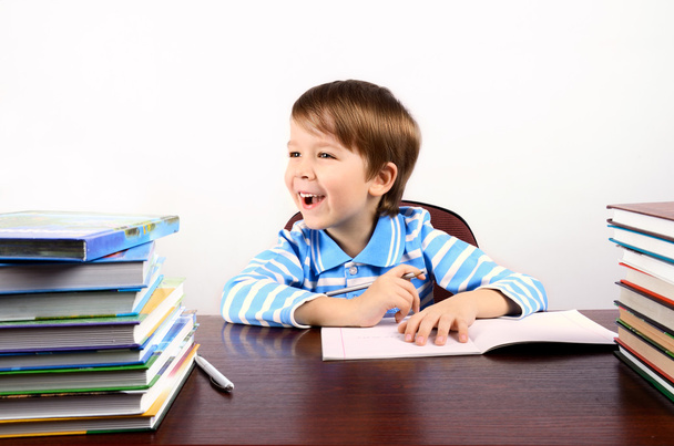 Хлопчик сміється сидить за столом з багатьма книгами
 - Фото, зображення