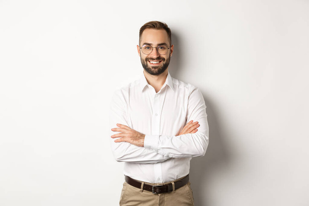 Business. Young professional businessman in glasses smiling at camera, cross arm on chest with confidence, standing over white background - Valokuva, kuva