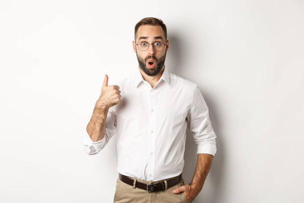 Impressed young male entrepreneur showing thumbs-up, praise something good, like and agree, white background - Photo, Image