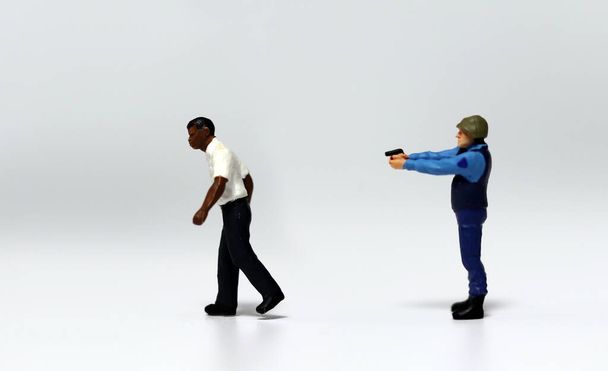 Une miniature de la police pointant une arme à l'arrière d'un homme miniature noir ambulant. Le concept de discrimination raciale par abus de pouvoir public. - Photo, image