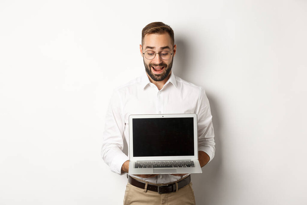 Возбужденный бизнесмен показывает что-то на экране ноутбука, стоя счастливым на белом фоне - Фото, изображение