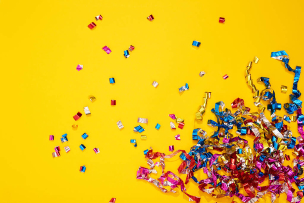 Colorful bright confetti and streamers on yellow background, top view. Copy space for text. Holiday mood, Christmas, New year, birthday or funny party. - Foto, immagini