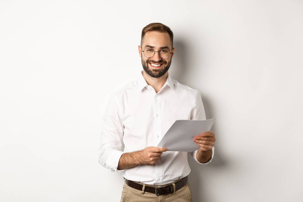Zaměstnavatel vypadá spokojeně s prací, čtení dokumentů a s úsměvem potěšen, stojící nad bílým pozadím - Fotografie, Obrázek