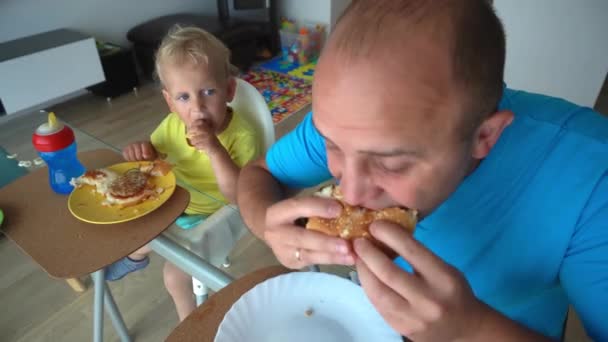 Éhes apa és fia hamburgert esznek. kameramozgás. - Felvétel, videó