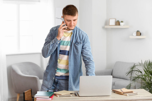 Młody człowiek rozmawiający przez telefon podczas korzystania z laptopa w domu - Zdjęcie, obraz