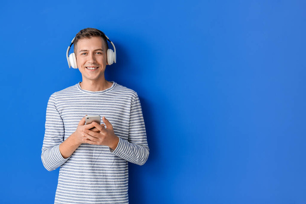 Young man with headphones and mobile phone on color background - Фото, зображення