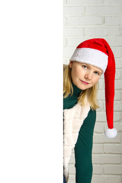 Різдвяна блондинка Санта, яка заглядає з-за порожнього знака рекламного щита, призначає білої цегляної стіни. Різдвяна дівчинка гном, копіювати простір
 - Фото, зображення