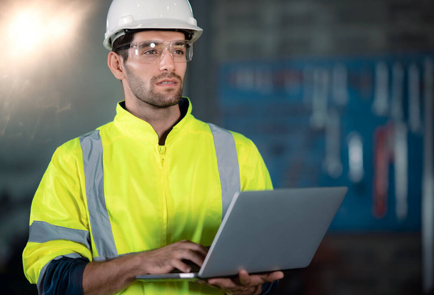 Chief Engineer in the Hard Hat Walks Through Light Modern Factory While Holding Laptop. Successful, Handsome Man in Modern Industrial Environment. - Foto, immagini