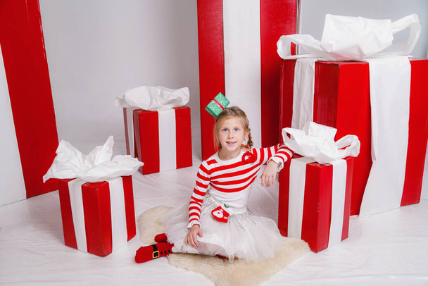 happy funny child girl in Christmas costume with big red gifts on background. - Foto, Imagem