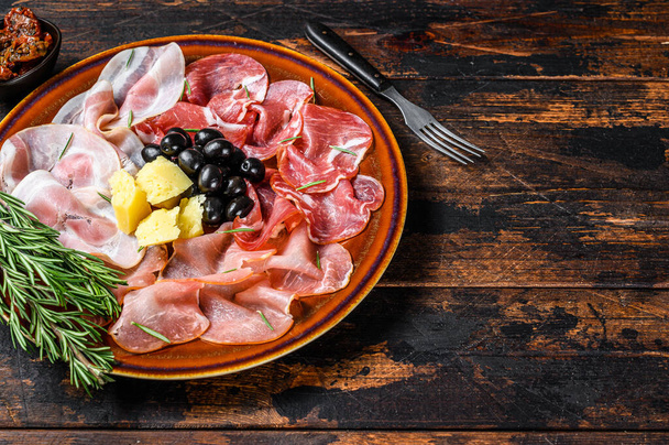 プロシュットハム、ブレザオラ、パンチェッタ、サラミ、パルメザンチーズとイタリアの肉のプレート。暗い木製の背景。最上階だ。スペースのコピー. - 写真・画像