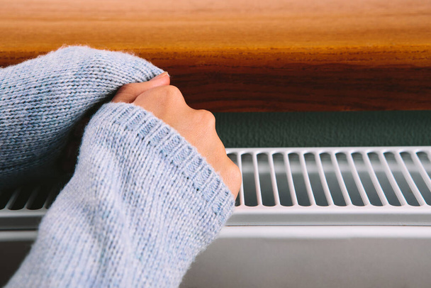 girl warms her hands and feet on a radiator - Φωτογραφία, εικόνα
