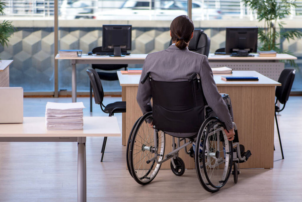 Молодой работник в инвалидной коляске работает в офисе - Фото, изображение