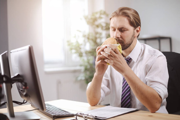 Empresario sentado en la oficina y comiendo hamburguesa - Foto, imagen
