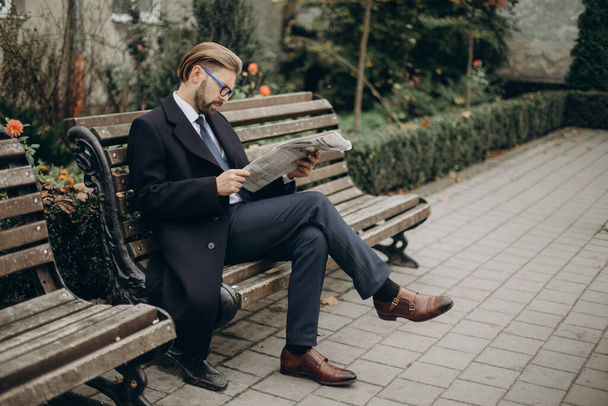 Бизнесмен читает газету на скамейке - Фото, изображение