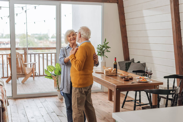 happy senior couple dancing near table with dinner at home - Foto, Bild