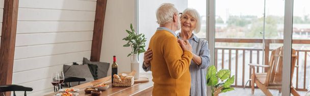 smiling elderly couple dancing near table with vegetarian dinner in kitchen, banner - Foto, immagini