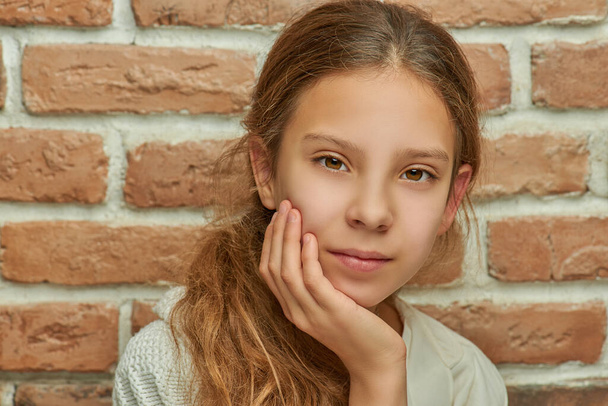Girl teenager with long hair looks thoughtfully against brick wall. - Photo, Image