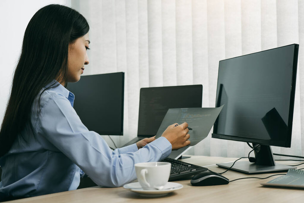 Mujer asiática desarrolladores de software sentado frente a los ordenadores mirando los códigos de ordenador en la pantalla. - Foto, imagen