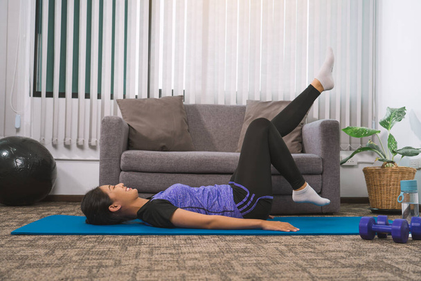 Aasialainen nainen harjoittelee joogaa kotona makaamassa matolla ja venyttelemässä jalkojaan. - Valokuva, kuva