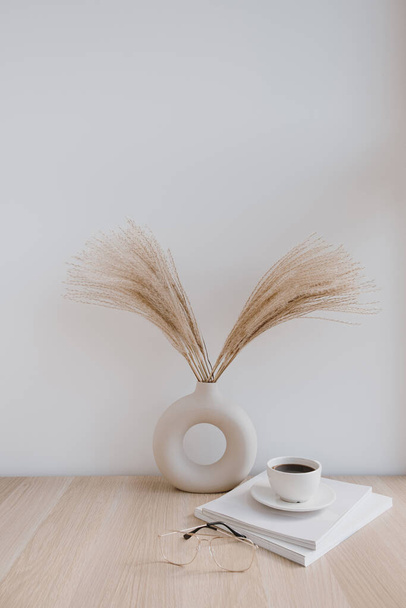 Pampas morbide erba / canna in vaso elegante, tazza di caffè, bicchieri e riviste contro parete bianca. Decorazione d'interni minimale. Concetto stilizzato per i blogger. Vibrazioni parigine. - Foto, immagini