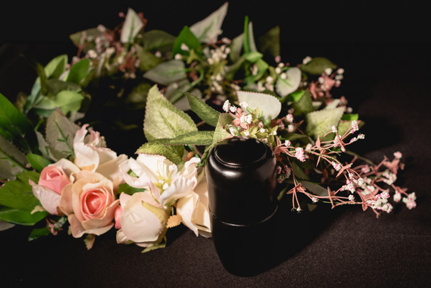 rose bouquet and urn with ashes on black background, funeral concept - Photo, Image