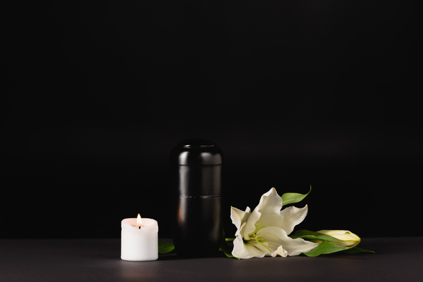 lily, candle and urn with ashes on black background, funeral concept - Photo, Image
