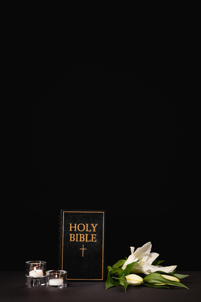 lily, candles and holy bible on black background, funeral concept - Foto, imagen