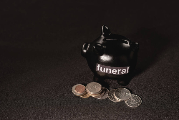 piggy bank with coins on black background, funeral concept - Photo, Image