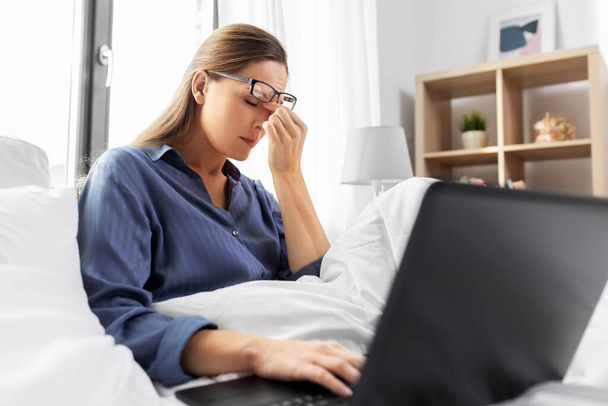 tired woman in glasses with laptop in bed at home - Foto, Imagen
