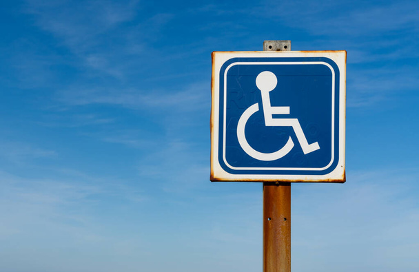 lähikuva vammaisen tai vammaisen pysäköintipaikan merkistä, jonka reunat ovat ruostuneet ja jonka takana on kopiotila ja sininen taivas - Valokuva, kuva