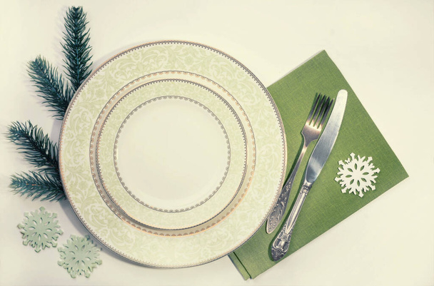 Tisch gedeckt. Teller, Gabel, Messer und grüne Serviette auf dem Tisch. Die festliche Tischdekoration des neuen Jahres. Weihnachtstisch gedeckt. Messer, Gabel und Teller mit Neujahrsdekoration - Foto, Bild