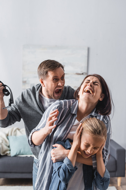 Crazy man holding waist belt near crying wife and child at home  - Fotoğraf, Görsel