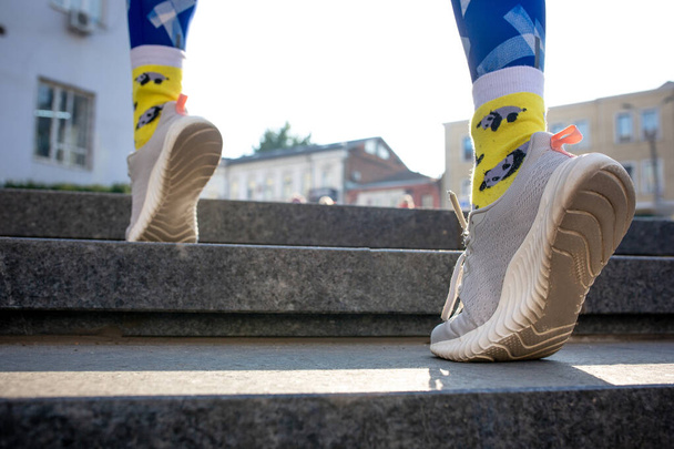 Gambe femminili close-up in leggins blu e calzini gialli che corrono di sopra all'aperto. - Foto, immagini