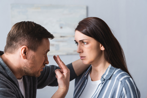 Pahoinpitelevä aviomies osoittaa silmiin lähelle vaimoa mustelmilla kotona  - Valokuva, kuva