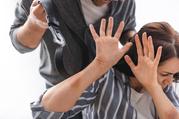 Επιθετικός σύζυγος κρατώντας ζώνη μέσης κοντά σε τρομαγμένη σύζυγο με μώλωπες στα χέρια  - Φωτογραφία, εικόνα