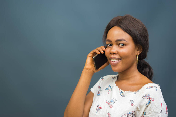 A closeup shot of a beautiful young African lady talking on her phone - Zdjęcie, obraz