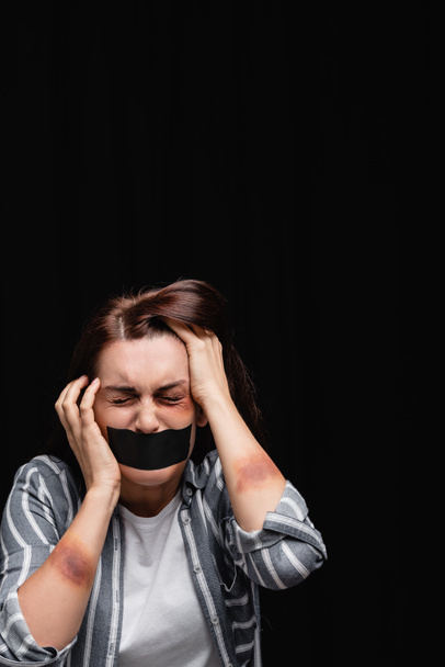 Депресивна жінка з синцями і клейкою стрічкою на роті ізольована на чорному
  - Фото, зображення