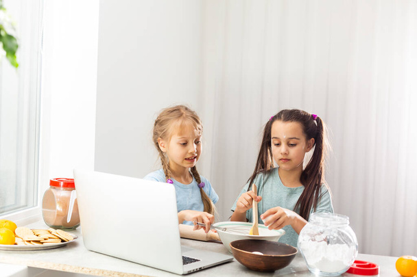 台所の2人の小さな女の子は、家族のためのデザートを準備します。彼らは料理を学ぶと、彼らは小麦粉で遊び始め、お互いに笑顔。概念：料理教室、家庭、教育. - 写真・画像