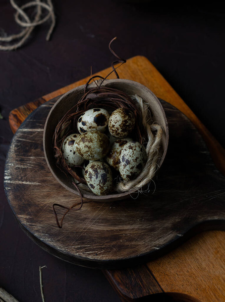 An overhead shot of speckled quail eggs with jute twine in a rustic bowl on a wooden board - Fotoğraf, Görsel