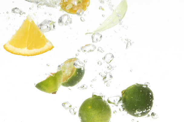 A closeup shot of lime and lemon slices dropping into water - Foto, Imagem