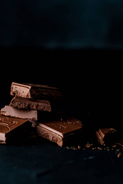 A vertical shot of chocolate bars broken into pieces in a dark room - 写真・画像
