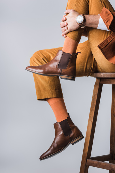 Cropped view of stylish man in brown shoes sitting on wooden chair isolated on grey  - Photo, Image