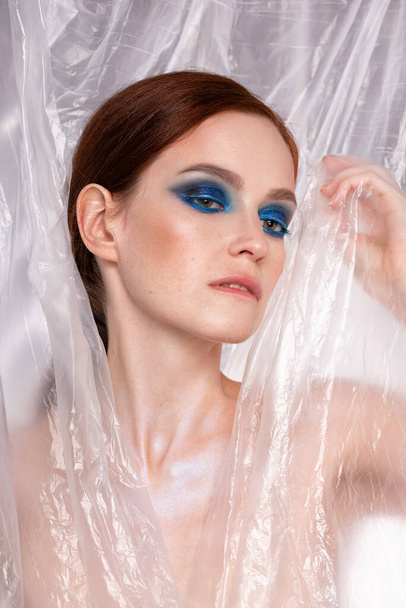 Retrato de moda de belleza de mujer pelirroja con ojos azules ahumados maquillaje. Brillo fondo abstracto - Foto, Imagen
