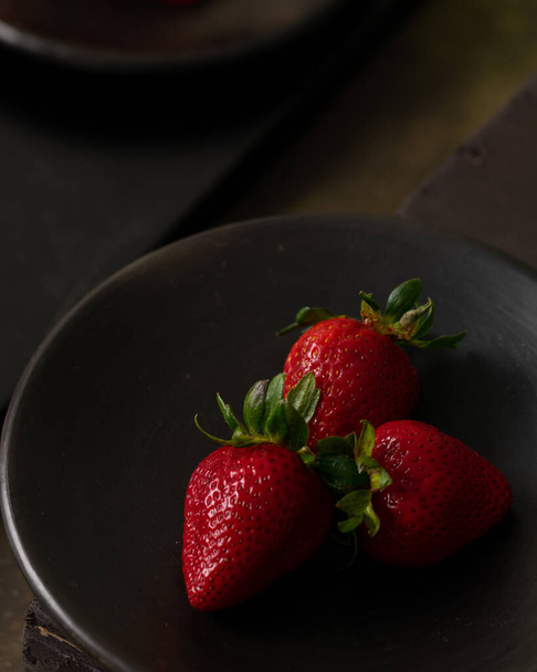 A closeup of red, fresh strawberries on a black plate - Foto, Imagen