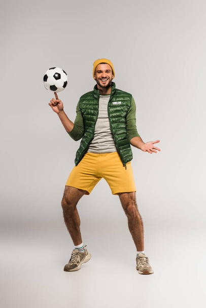Sportsman smiling at camera while holding football on finger on grey background  - Foto, imagen