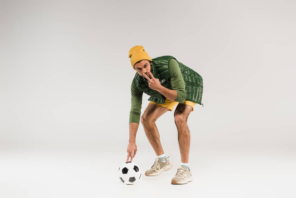 Sportsman tenendo il calcio e puntando con le dita agli occhi su sfondo grigio  - Foto, immagini
