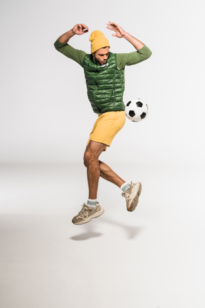 Excited sportsman jumping while playing football on grey background  - Φωτογραφία, εικόνα