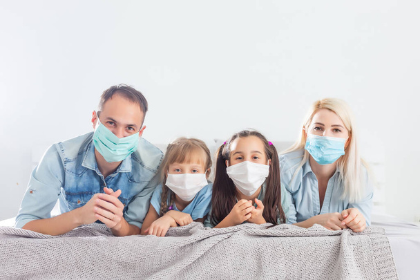 Aile karantinada, ev hapsindeyken koronavirüs, karı koca ve çocuklar yatakta, aile maskeli. - Fotoğraf, Görsel
