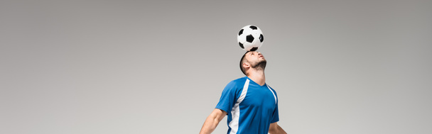 Kafasında futbol topu tutan genç sporcu gri pankartta tek başına.  - Fotoğraf, Görsel
