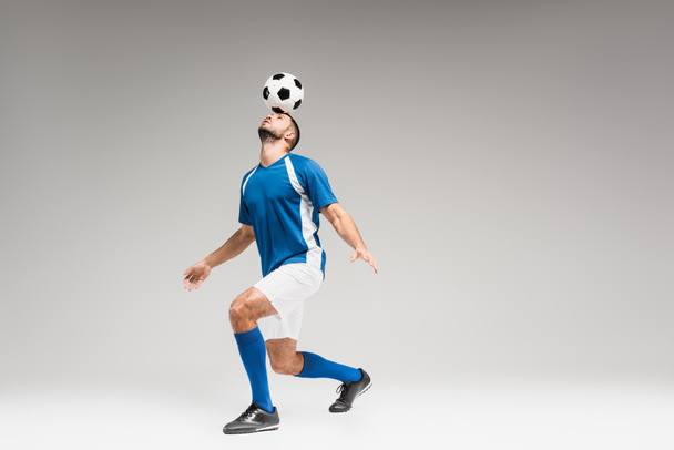 Sportsman holding football on head while balancing on grey background  - Valokuva, kuva